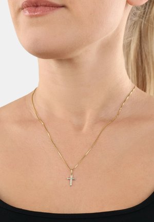 Goldene Kettenhalskette mit einem kleinen Kreuzanhänger, verziert mit einem klaren Edelstein in der Mitte, auf einem schwarzen Oberteil.