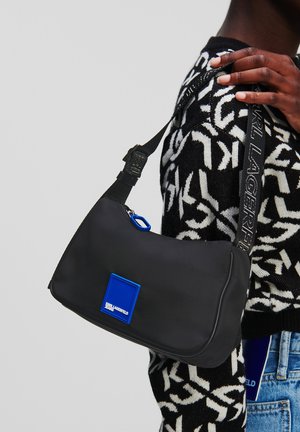 Borsa a spalla nera in nylon con forma curva, toppa del logo blu, tracolla regolabile con branding e chiusura con zip.