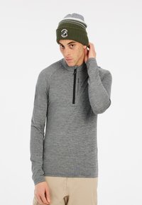 Grijze lange mouwen pullover met een kwart-rits en raglanmouwen. Het model draagt een groene gebreide muts met een logo en witte strepen.