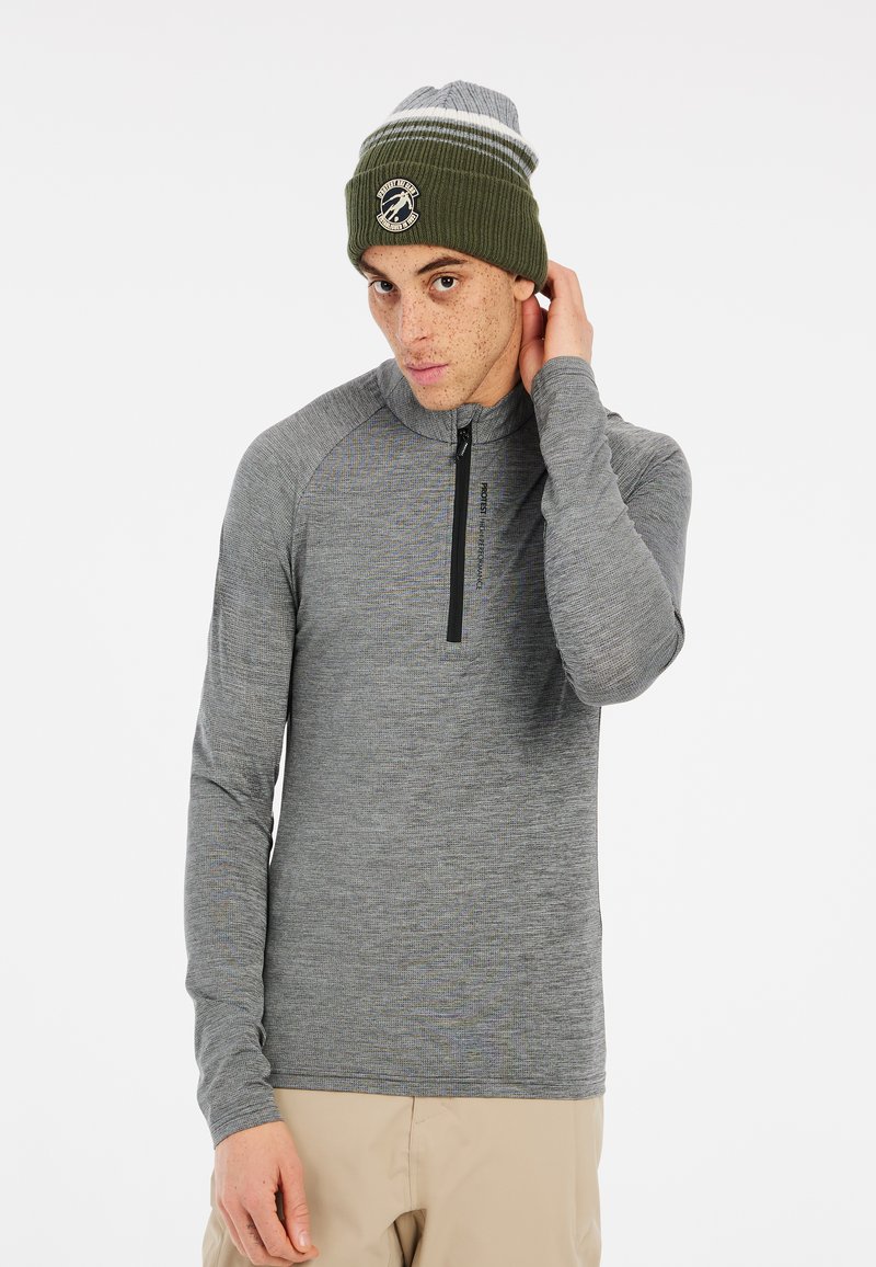 Grijze lange mouwen pullover met een kwart-rits en raglanmouwen. Het model draagt een groene gebreide muts met een logo en witte strepen.