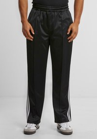 Black sports pants made of smooth, synthetic material, with elastic waistband, featuring white side stripes and a straight-leg design.