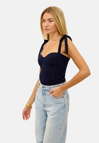 Un body marine avec des rayures fines, un col structuré et des bretelles à nouer. Assorti à un jean taille haute bleu clair et un bracelet en or.