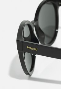 Mustad musta raamiga prillid tumedate läätsedega, millel on läikiv viimistlus. Raam on ümarate kujundite ja küljel on kuldse kirjaga "Polaroid".