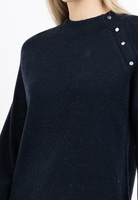 Marineblauer Pulli mit Rundhalsausschnitt, aus weichem Stoff. Verfügt über eine strukturierte Oberfläche und silberne Druckknopfdetails an der Schulter.