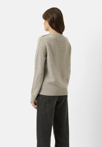 Maglione lavorato a maglia grigio chiaro con scollatura rotonda, polsini e orlo ribattuti, e una vestibilità rilassata, abbinato a jeans neri a gamba larga.