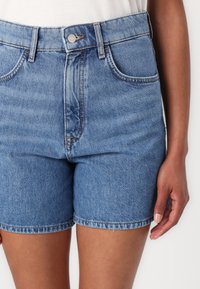 Lys blåvaskede denimshorts med høj talje, forlommer, metalspænde og sticheret kant. Glat tekstur.