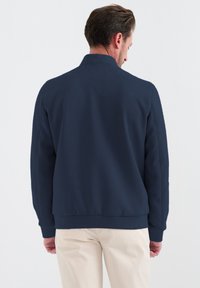 Mörkblå bomberjacka med en mjuk textur, med krage, ribbade muddar och en åtsittande midja. Designad för avslappnad användning.