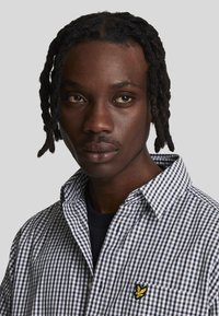 Camicia a quadri bianco e nero con colletto button-up, dotata di un logo ricamato giallo sulla tasca del petto.