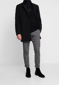 Svart ytterrock, stickad svart tröja och grå rutiga byxor. Avslutat med svarta mocka ankle boots. Slät tyg och skräddarsydd passform.