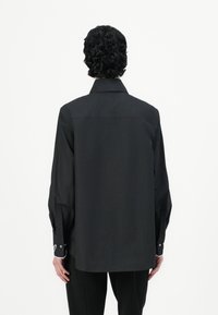 Camicia nera a maniche lunghe realizzata in tessuto morbido, caratterizzata da un colletto standard, polsini abbottonati e un taglio dritto, con un logo discreto sul retro.