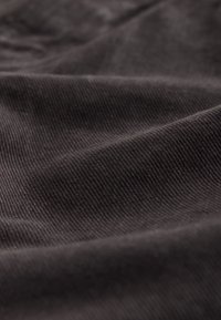 Gros plan d'un tissu côtelé brun foncé montrant un motif de tissage diagonal et des plis doux.