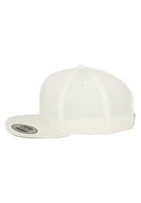 White baseball cap with a flat brim, structured crown, and mesh panels. Features a circular logo patch on the underside of the brim.