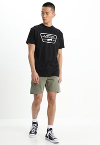 Svart t-shirt i bomull med vitt grafiskt logotyp, i kombination med olivgröna cargoshorts och svarta höga sneakers.