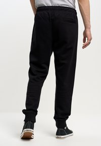 Zwarte joggingsbroek van zachte stof met een elastische tailleband, omgeslagen enkels en een enkele achterzak. Draag met zwarte sneakers.