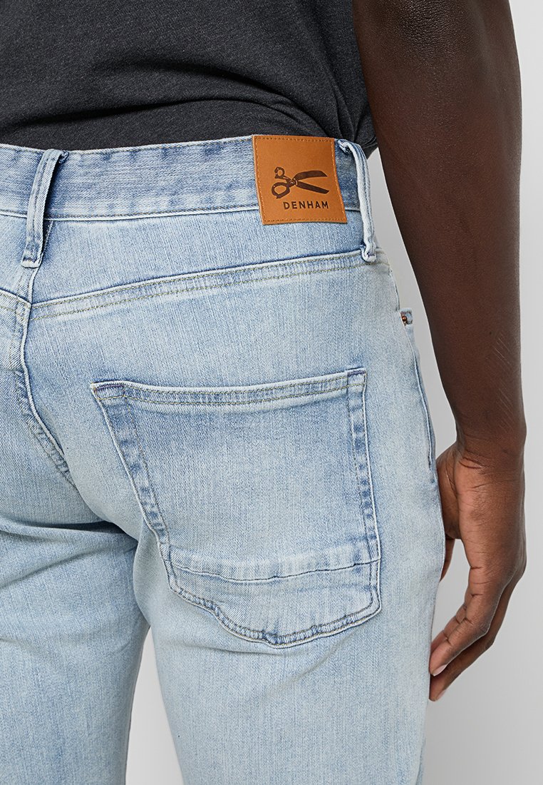 Lichtblauwe denim jeans met een leren label van "DENHAM" op de achterste tailleband, met standaardzakken en een aangesloten ontwerp.