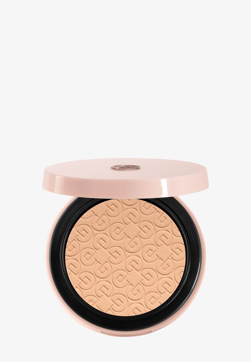 Poudre compacte beige pressée avec un motif géométrique embossé, contenue dans un boîtier rond rose pâle avec un couvercle partiellement ouvert.