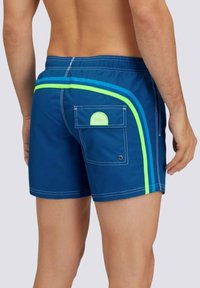 Pantaloni da nuoto blu con strisce a contrasto di blu chiaro e verde neon, dotati di una tasca sul retro e di una toppa con logo circolare.