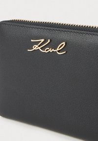 Portofel negru din piele cu logo-ul auriu "Karl", având o suprafață texturată și fermoar auriu. Accent pe linii curate și design minimalist.