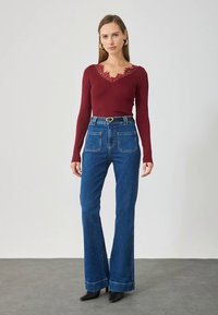 Burgunderfarget ribbestrikket langermet topp med blondedetaljer ved halsen, kombinert med høytlivs blå vide jeans og svarte støvletter med hæl.