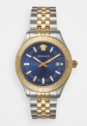 Montre en acier inoxydable doré et argenté avec un cadran bleu, un design complexe, de grands chiffres pour les heures et une fenêtre de date à 3 heures.