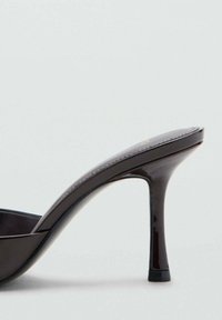 Sandalia negra de tacón alto con acabado brillante, diseño de punta abierta, correa curva elegante y un delgado tacón de aguja. Suela plana con acentos mínimos.
