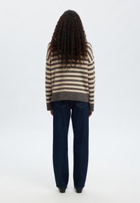 Csíkos pulóver bézs és sötétszürke színben, laza szabással és rövidített szegéllyel. Magas derekú, bő szárú sötét farmernadrággal párosítva.