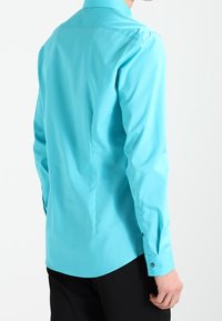 Lichtblauw overhemd met lange mouwen, een gladde textuur, knoopmanchetten en een klassieke kraag, weergegeven van achteren tegen een witte achtergrond.