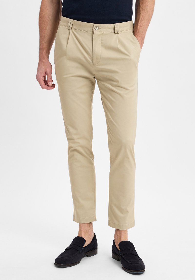 Beige chino's met een slim fit, voorzien van een rechte voorkant, riemlussen en een knoopsluiting; gecombineerd met zwarte suède loafers.
