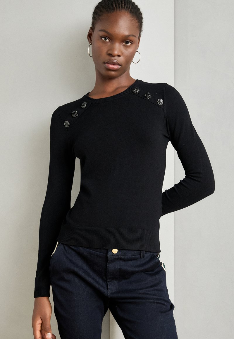 Černý pletený svetr s kulatým výstřihem a dekorativními knoflíky na ramenou. Materiál vypadá hladce a má přiléhavý střih.