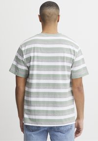 Camiseta de manga corta y cuello redondo con rayas horizontales verdes y blancas, hecha de una tela suave y con un corte relajado, vista desde la parte posterior.
