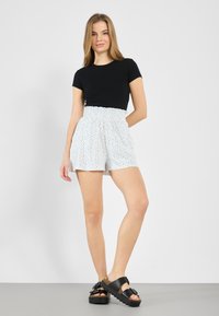 Black fitted short-sleeve top paired with white floral print shorts, featuring a ruffled waistband. Worn with black platform sandals.