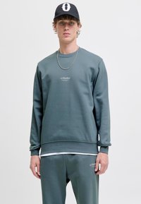Grijze, gestructureerde sweatshirt met een geribbelde onderrand. Beschikt over een subtiel logo op de borst en is gecombineerd met bijpassende joggers.