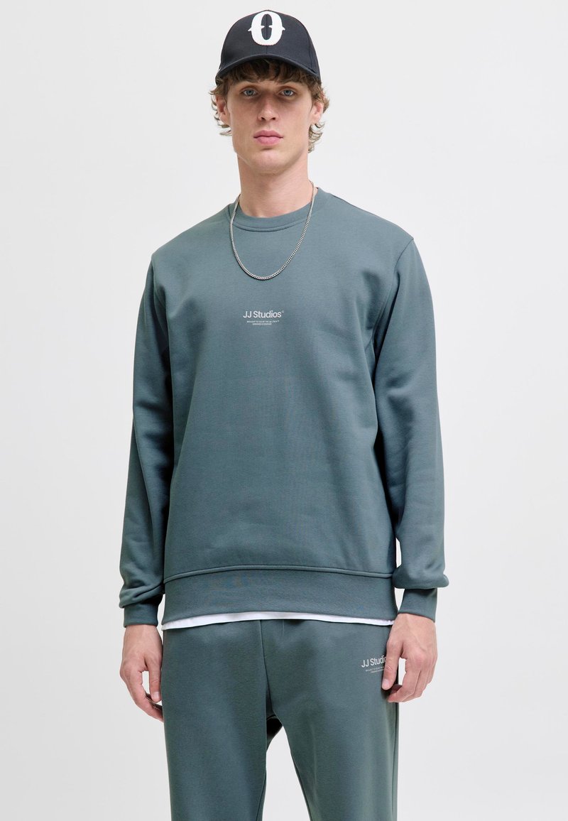 Grijze, gestructureerde sweatshirt met een geribbelde onderrand. Beschikt over een subtiel logo op de borst en is gecombineerd met bijpassende joggers.