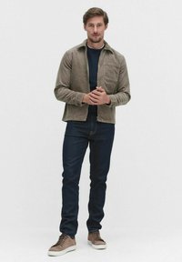 Brown corduroy jacket, navy crew neck shirt, dark jeans, and light brown sneakers. Jacket features a front pocket and zipper closure.