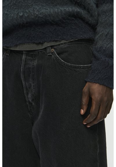 Zwarte denim jeans met een losse pasvorm, vijf zakken en contrasterende stiksels. Het materiaal lijkt stevig met een subtiele textuur.