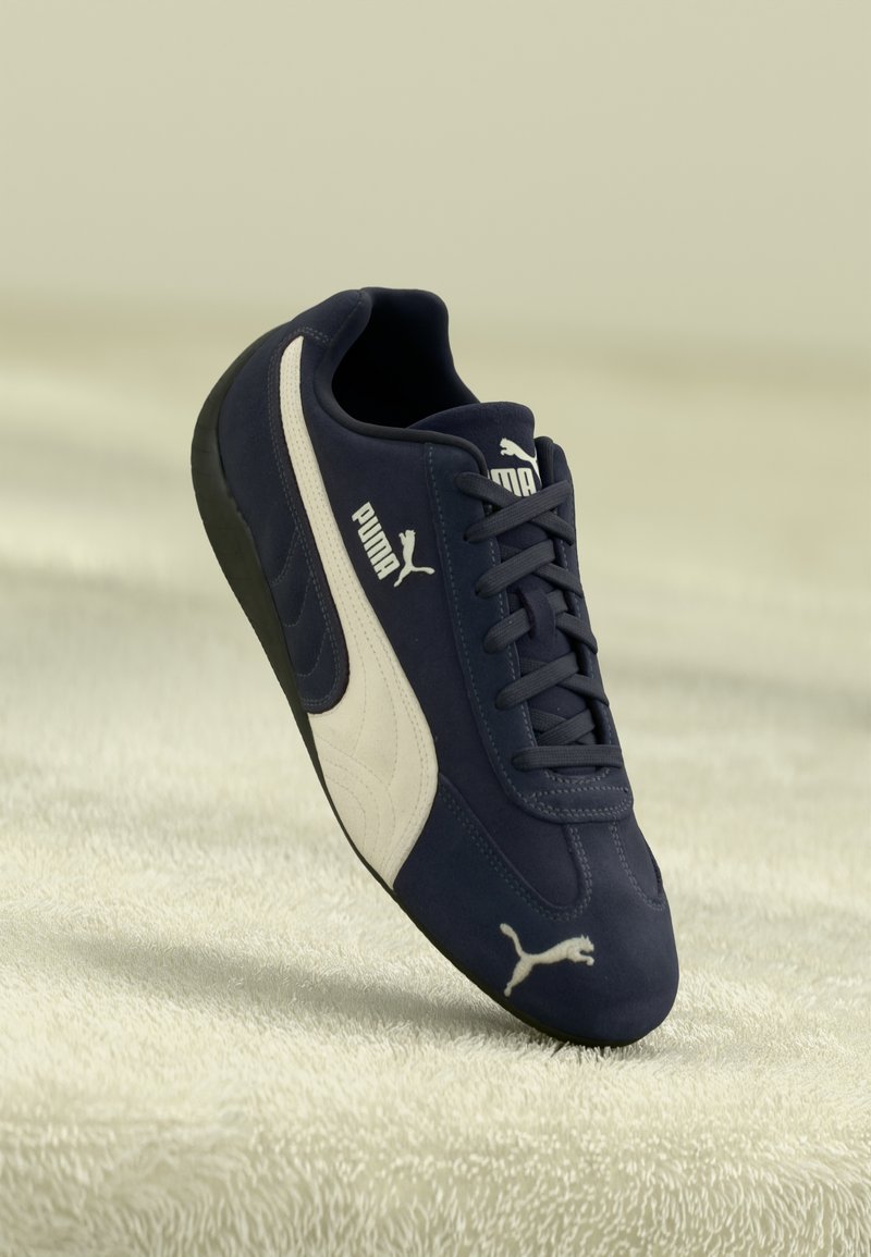 Marineblå sneakers med en glat, ruskindsagtig overflade, med et hvidt Puma-logo og accentstribe. De har en rund tå og sort sål.