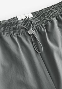 Gray, lightweight fabric with a gathered waistband, featuring a drawstring and a metal adjustment toggle. Label reads "Self." Smooth texture.