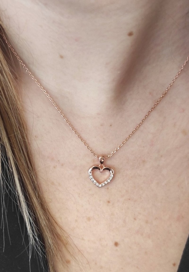 Collana in oro rosa con un pendente a forma di cuore impreziosito da pietre trasparenti, appesa a una delicata catena, poggiata sulla pelle.