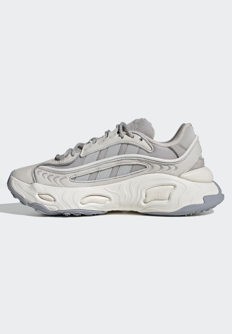 Graue Sneaker mit strukturiertem Obermaterial, geschichtetem Design und drei Streifen an der Seite. Verfügt über eine klobige weiße Zwischensohle mit gewellten Mustern.