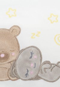 Gesticktes Bärenmotiv in sanftem Beige und Grau auf weißem Stoff, mit plüschiger Textur, rosa Akzenten und gelben Sternen im Hintergrund.