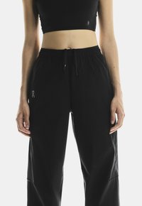 Black jogger pants with an elastic waistband and adjustable drawstring. Features side pockets and a reflective logo on the left leg.