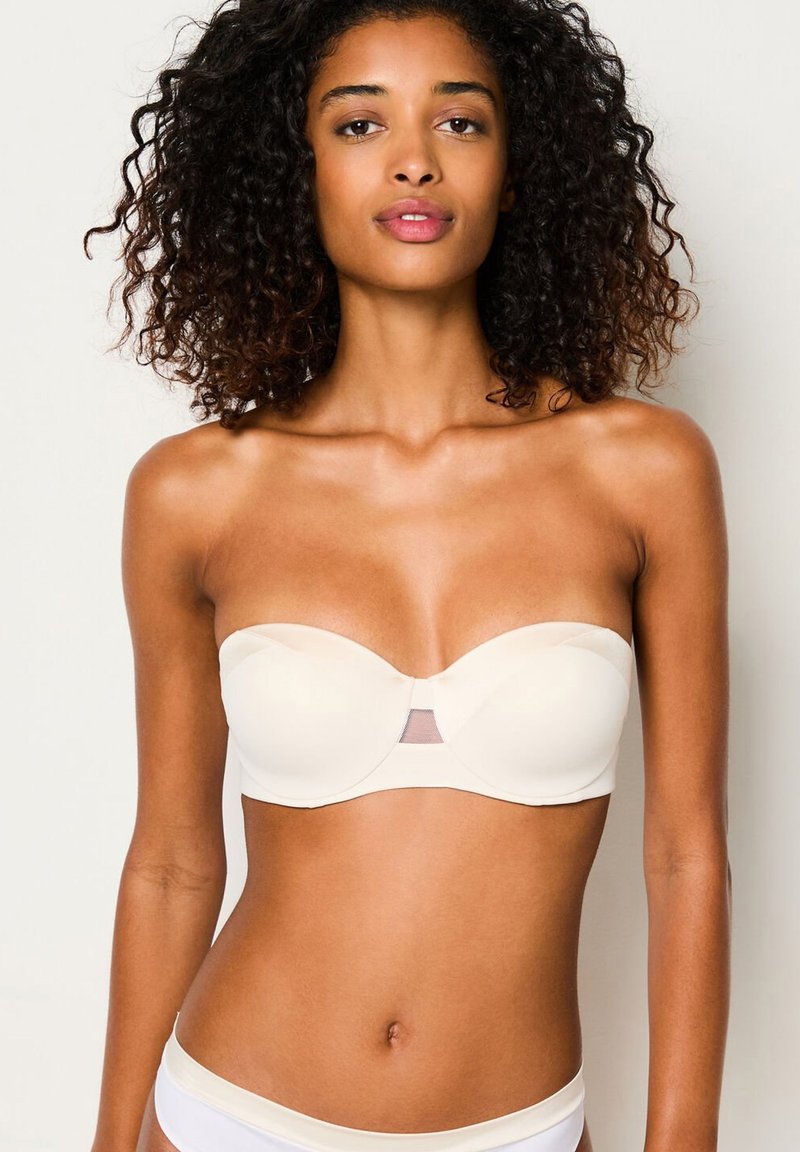 Reggiseno senza spalline in morbido tessuto beige chiaro con una texture liscia. Presenta un pannello in rete al centro e coppe sagomate per il supporto.