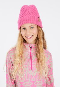 Un bonnet en tricot rose avec un motif texturé, associé à un haut zippé à motifs dans des teintes pastel de rose et de beige.