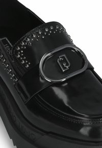 Zwarte gepatenteerde leren loafer met studaccents, een oversized metalen gesp en een dikke zwarte rubberen zool met merklogo.