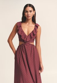 Abito bordeaux con pois bianchi; presenta bordi arricciati, scollatura a V profonda, vita con taglio e una vita elasticizzata per una vestibilità comoda.