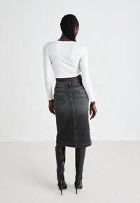 Gonna midi in denim nero con taglio dritto, tasche posteriori e vita. Indossata con stivali neri alti con tacco e un crop top bianco.