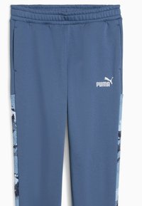 Pantalones deportivos azules con cintura elástica, que presentan un patrón de estilo camuflaje en los paneles laterales y un logo de Puma blanco en la parte frontal.