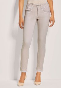 Lichtbeige skinny jeans van denim, met studded pocketaccenten en een rafelige zoom. Gecombineerd met nude kleurige hakken.