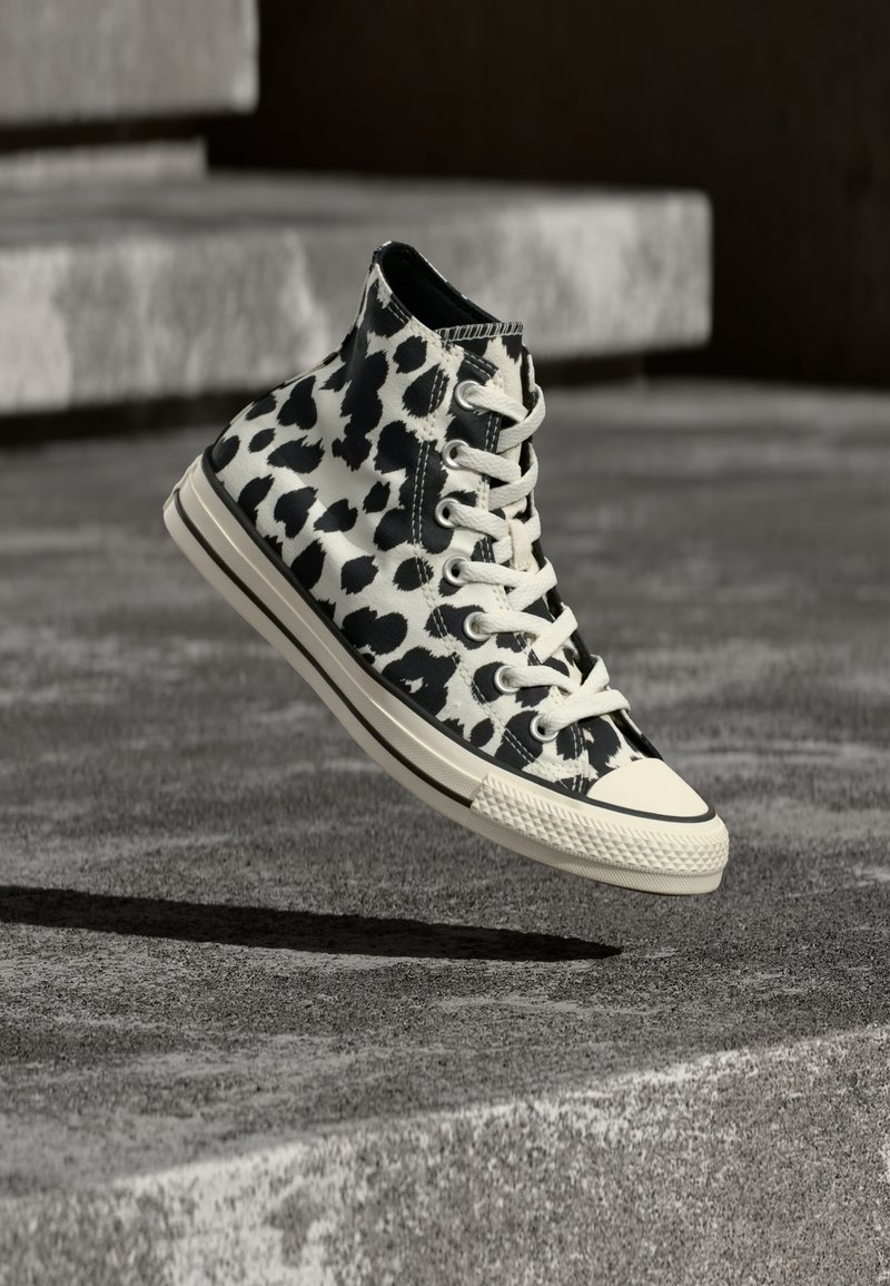 Ανδρικό αθλητικό παπούτσι σε κοντό ύψος, ασπρόμαυρο με σχέδιο λεοπάρδαλης, λευκά κορδόνια και κρεμ λαστιχένια σόλα που αιωρείται πάνω από επιφάνεια από σκυρόδεμα.