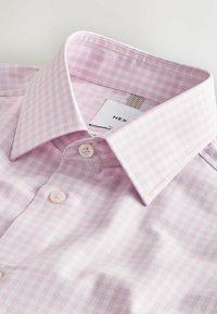 Chemise à carreaux roses et blancs avec col large et deux boutons blancs attachés près du haut.